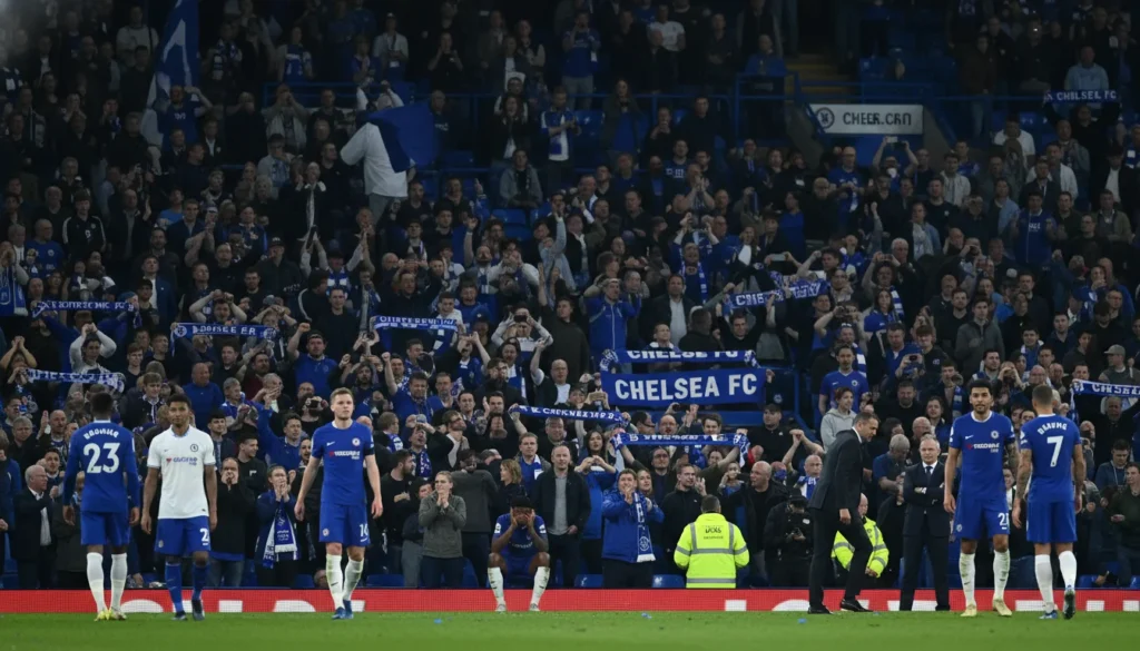 Chelsea demite Enzo Maresca seis meses após título mundial: Entenda os motivos da decisão chocante Cena do estádio do Chelsea lotado após derrota, jogadores desanimados e torcida frustrada, cores azul e branco